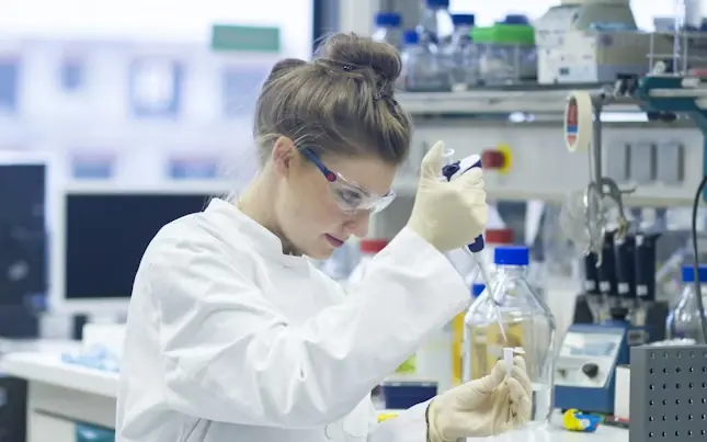 Scientist in a white coat using a pipette at a laboratory bench